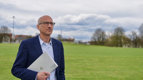 Un uomo è al parco con un portatile sotto il braccio e guarda il cielo nuvoloso.