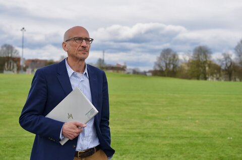 Un uomo è al parco con un portatile sotto il braccio e guarda il cielo nuvoloso.