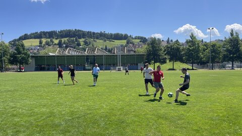 Zwei Frauen und sechs Männer spielen auf dem Rasen Fussball.