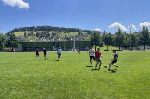 Zwei Frauen und sechs Männer spielen auf dem Rasen Fussball.